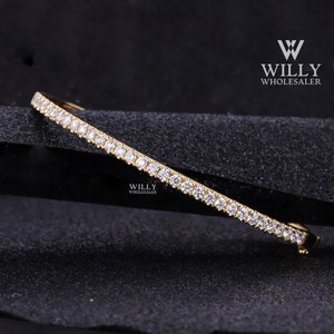 May include: A gold bangle bracelet with a row of small, clear diamonds set in a continuous line around the band.