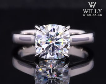 May include: A silver ring with a large, clear, cushion-cut diamond. The ring is set on a plain band with a slightly raised edge.