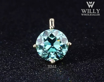 May include: A teal blue gemstone pendant with a gold setting. The gemstone is round and has a faceted cut. The pendant is on a black background.