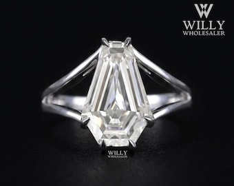 May include: A silver-toned ring featuring a large, clear, coffin-shaped faceted gemstone set in a prong setting. The band is split into two distinct arms that meet at the base of the stone. The text WILLY WHOLESALER is visible in the corner.