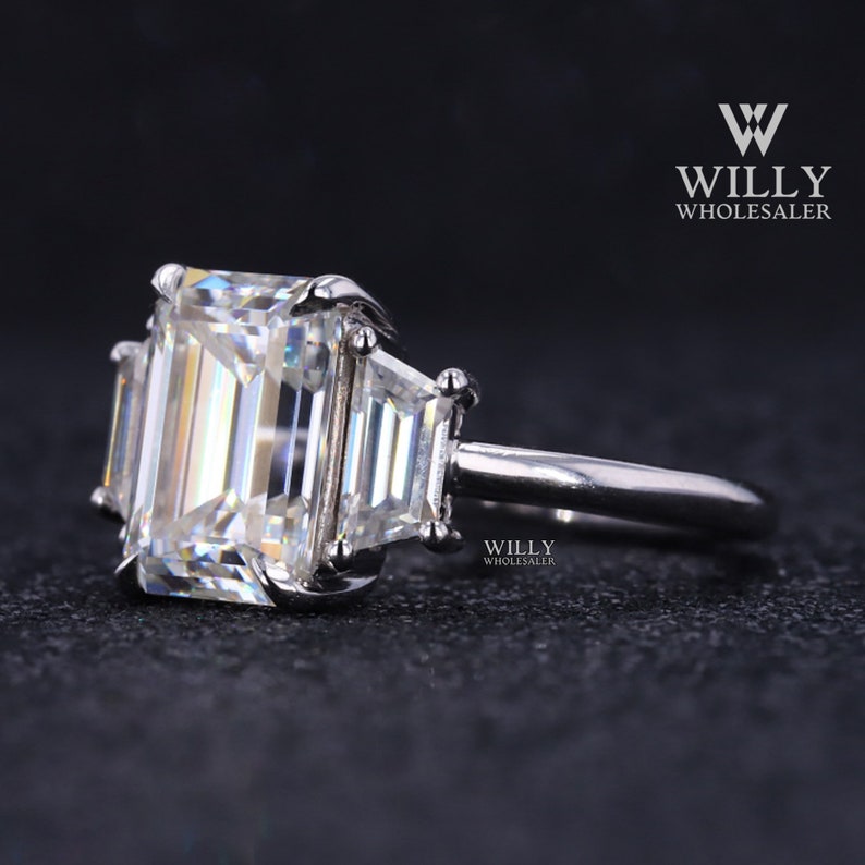 May include: A silver ring with a large emerald-cut diamond center stone and two smaller baguette-cut diamonds on either side.