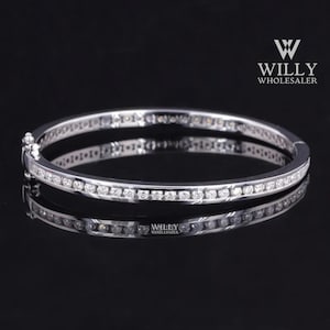 May include: A silver bracelet with a row of small, clear gemstones set along the top and bottom edges. The bracelet is displayed on a reflective black surface, with the brand name "WILLY WHOLESALER" visible in the upper right corner.