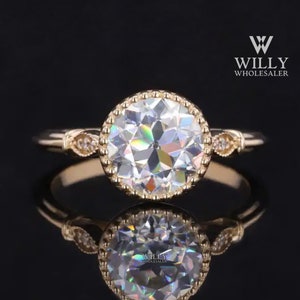May include: A gold engagement ring with a large, round, faceted diamond set in a bezel setting with a decorative border. The ring has a delicate band with small diamonds on each side.