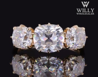 Puede incluir: Un anillo de oro con tres grandes piedras preciosas transparentes de talla cojín. El anillo está engastado con una piedra central flanqueada por dos piedras más pequeñas.