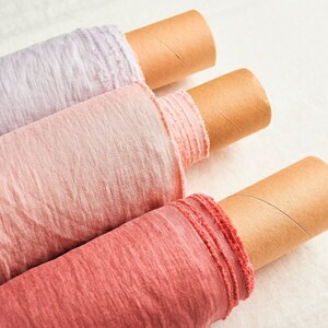 May include: Three rolls of fabric in different shades of pink, from light to dark, are rolled up on cardboard tubes. The fabric has a soft, textured look.