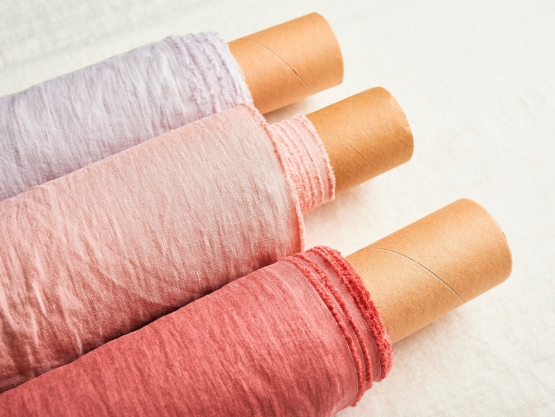 May include: Three rolls of fabric in different shades of pink, from light to dark, are rolled up on cardboard tubes. The fabric has a soft, textured look.