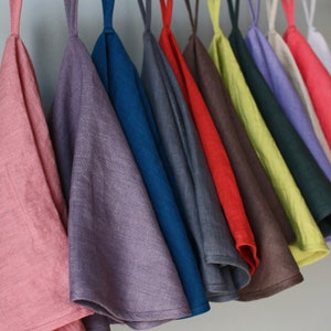May include: A set of 12 linen tea towels hanging on a wooden rod. The towels are in various colors, including pink, purple, blue, gray, red, brown, yellow, green, and lavender.