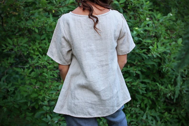 May include: A light beige linen top with a scoop neck and short sleeves. The top is loose fitting and has a slightly A-line shape.