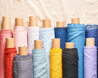 May include: A collection of fabric rolls in various colors, including red, pink, light blue, yellow, and purple. The fabric rolls are arranged in a row on a beige surface.