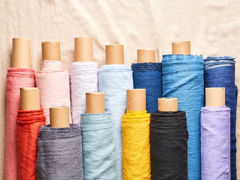 May include: A collection of fabric rolls in various colors, including red, pink, light blue, yellow, and purple. The fabric rolls are arranged in a row on a beige surface.