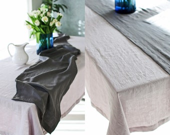 May include: A light pink linen tablecloth with a gray linen table runner. The table runner is folded in half and placed lengthwise down the center of the tablecloth.