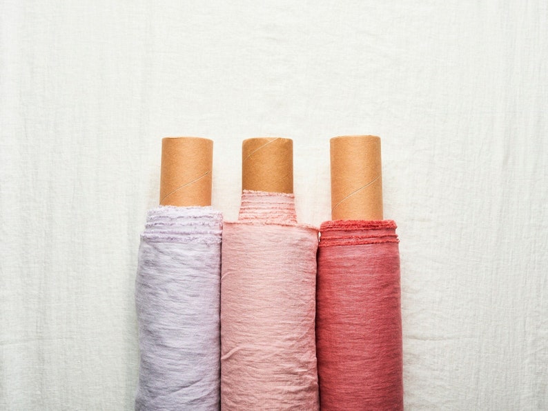 May include: Three rolls of fabric in different shades of pink, lavender, and red, each wrapped in brown paper.