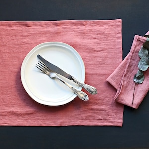 Könnte beinhalten: Ein rosa Leinen-Platzset mit einem weißen Teller, einer silbernen Gabel und einem silbernen Messer. Rechts im Bild liegt eine gefaltete rosa Leinen-Serviette mit einem Zweig Eukalyptus.