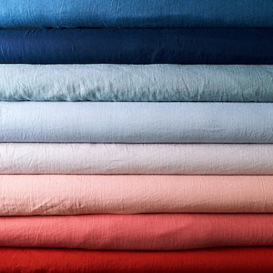 May include: A stack of fabric rolls in various shades of blue, light blue, white, pink, red, and orange. The fabric is a linen blend and has a textured surface.