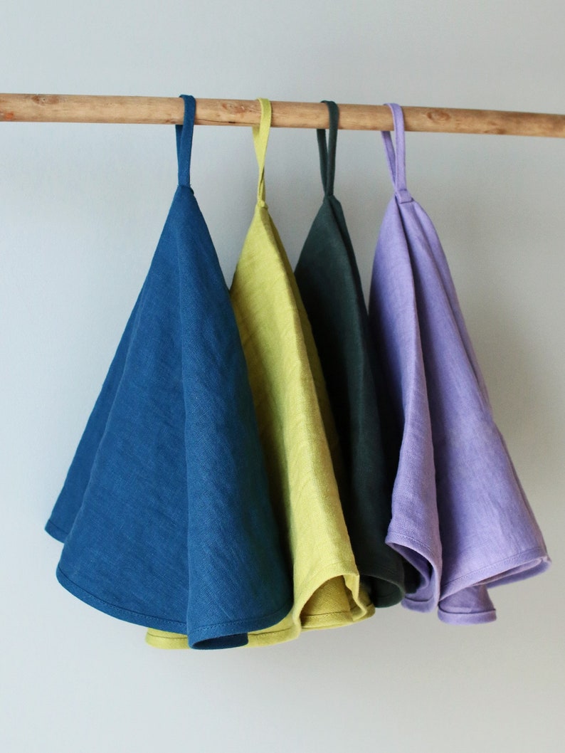 May include: Four linen tea towels hanging on a wooden rod. The towels are in shades of blue, green, yellow, and purple.