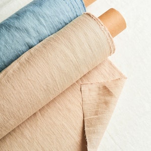 May include: Two rolls of fabric, one beige and one light blue, are rolled up and stacked on top of each other. The fabric is textured and has a linen look.