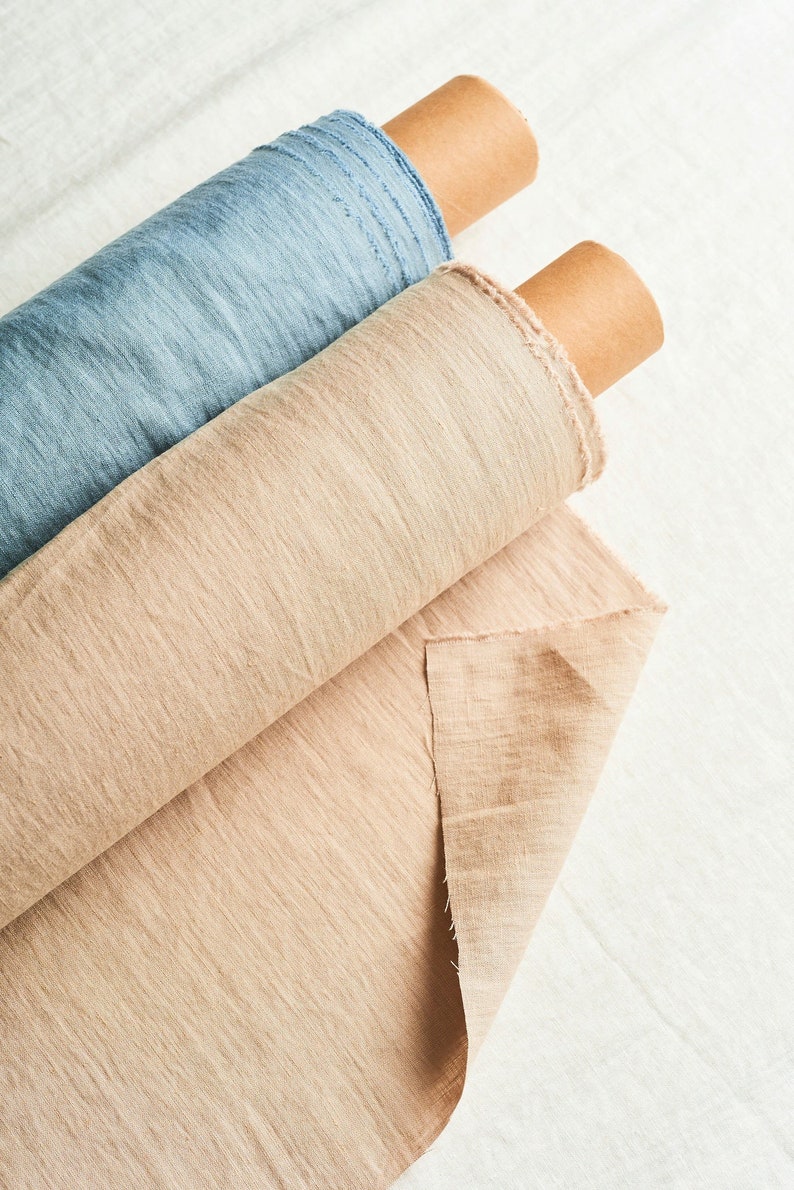 May include: Two rolls of fabric, one beige and one light blue, are rolled up and stacked on top of each other. The fabric is textured and has a linen look.