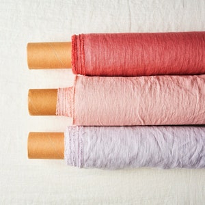 May include: Three rolls of fabric in different shades of pink and purple. The fabric is rolled up and secured with cardboard tubes. The fabric is a linen blend.