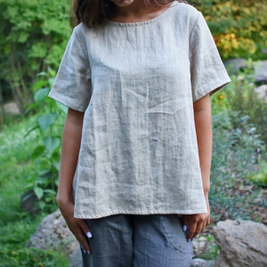 May include: A light beige linen top with short sleeves and a relaxed fit.