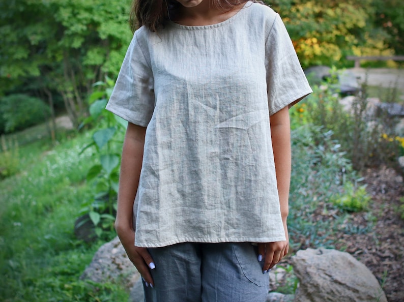 May include: A light beige linen top with short sleeves and a relaxed fit.