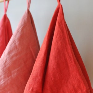 May include: Three linen tea towels hanging on a wooden rod. The towels are in shades of pink and red.