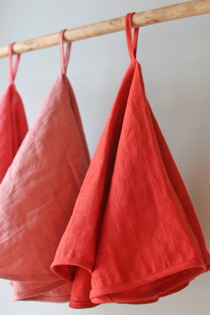 May include: Three linen tea towels hanging on a wooden rod. The towels are in shades of pink and red.