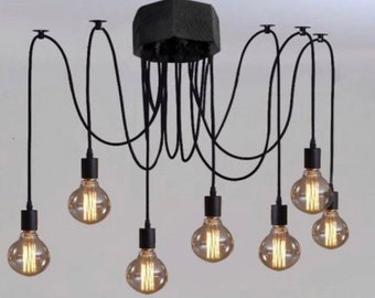 May include: Black spider-style chandelier with eight Edison-style light bulbs. The fixture has a central black wooden block with multiple black cords extending to the bulbs. The bulbs are round and have a warm, yellow glow.
