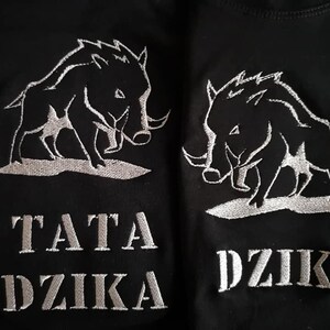May include: Two black t-shirts with white embroidered images of wild boars and the text "TATA DZIKA" and "DZIK" on the front.
