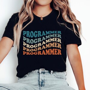 May include: A black t-shirt with the word "PROGRAMMER" repeated five times in a rainbow pattern. The text is in a retro font style.