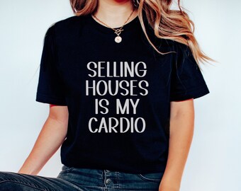 May include: A woman wearing a black t-shirt with the text "SELLING HOUSES IS MY CARDIO" in white lettering. She is wearing blue jeans and white sneakers.