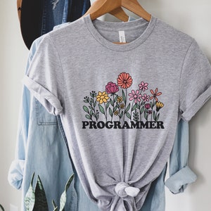May include: A gray t-shirt with a graphic of colorful flowers and the word "PROGRAMMER" in black letters.