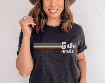 May include: A dark grey t-shirt with a retro design featuring colorful stripes and the text "5th grade".