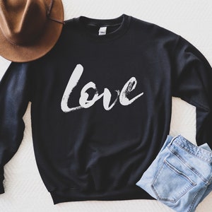 Puede incluir: Sudadera negra con la palabra "Love" escrita en letras blancas que parecen pintura.