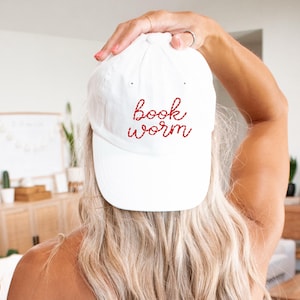 May include: White baseball cap with red embroidered text that reads "book worm".