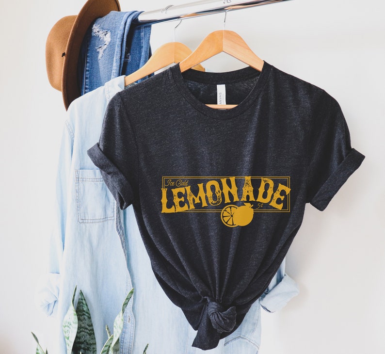 K&ouml;nnte beinhalten: Ein dunkelgraues T-Shirt mit einer gelben Grafik, auf der "Ice Cold Lemonade" mit einer Zitronenscheibe steht.
