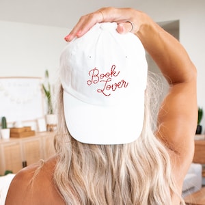 May include: White baseball cap with red embroidered text that reads "Book Lover".