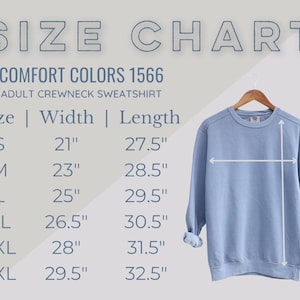 May include: A light blue adult crewneck sweatshirt hanging on a wooden hanger. The image includes a size chart with measurements in inches for sizes S, M, L, XL, 2XL, and 3XL. The text reads "SIZE CHART" and "COMFORT COLORS 1566".