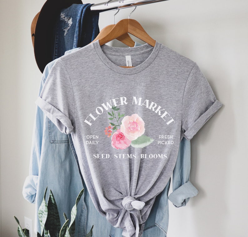 May include: Gray t-shirt with a white graphic that says "Flower Market" with a floral design and the text "Open Daily, Fresh Picked, Seed, Stems, Blooms."