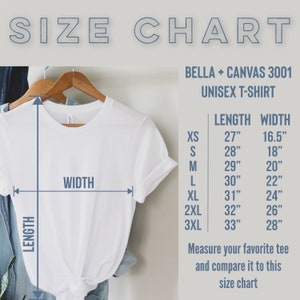 Może przedstawiać: Biała koszulka unisex Bella + Canvas 3001 na drewnianym wieszaku. Obraz zawiera tabelę rozmiar&oacute;w z wymiarami długości i szerokości w calach dla rozmiar&oacute;w XS do 3XL. U g&oacute;ry znajduje się napis "SIZE CHART".