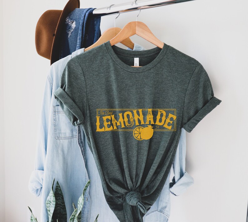 K&ouml;nnte beinhalten: Ein dunkelgr&uuml;nes T-Shirt mit einer gelben Grafik, auf der "Ice Cold Lemonade" mit einer Zitronenscheibe und einem Stern steht.