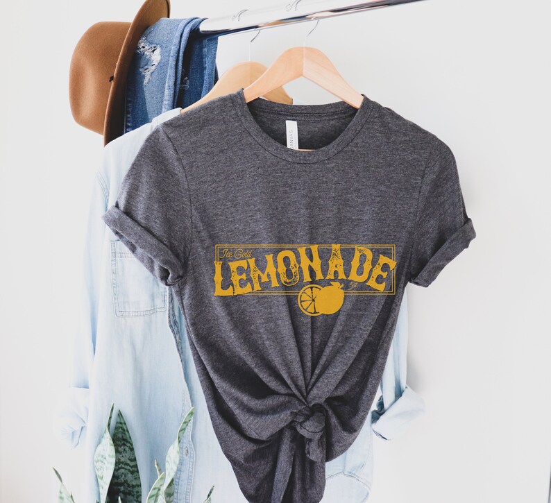 K&ouml;nnte beinhalten: Ein dunkelgraues T-Shirt mit einer gelben Grafik, auf der "Ice Cold Lemonade" mit einer Zitronenscheiben-Illustration steht.