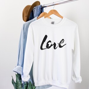 Puede incluir: Sudadera blanca con letras negras en forma de pinceladas que dicen "Love" en la parte delantera.
