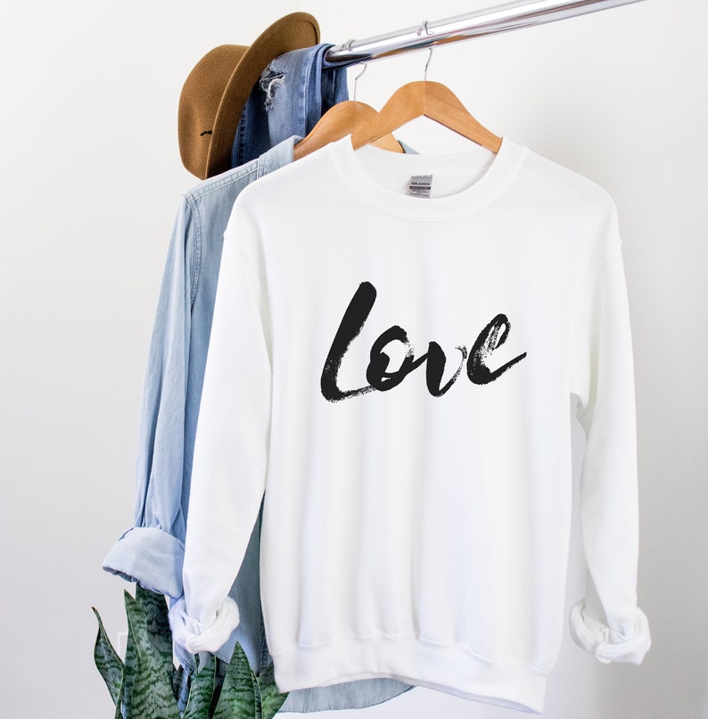 Puede incluir: Sudadera blanca con letras negras en forma de pinceladas que dicen "Love" en la parte delantera.