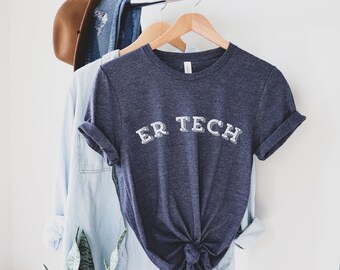 May include: A dark blue t-shirt with the text "ER TECH" in white lettering. The shirt is hanging on a wooden hanger.
