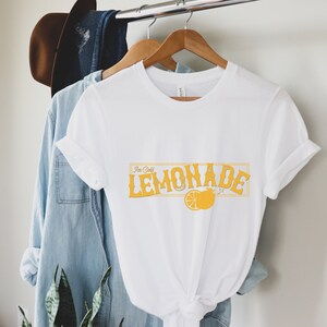 K&ouml;nnte beinhalten: Wei&szlig;es T-Shirt mit einer gelben Grafik, auf der "Ice Cold Lemonade" mit einer Zitronenillustration steht.
