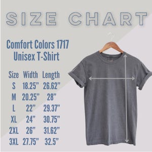 May include: A gray Comfort Colors 1717 unisex t-shirt displayed on a hanger. The image includes a size chart with measurements in inches: S (18.25" width, 26.62" length), M (20.25" width, 28" length), L (22" width, 29.37" length), XL (24" width, 30.75" length), 2XL (26" width, 31.62" length), and 3XL (27.75" width, 32.5" length).