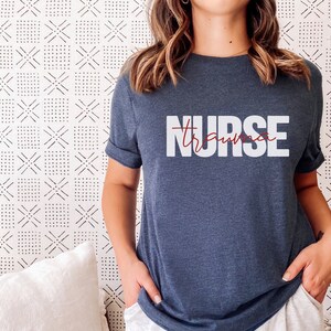May include: A navy blue t-shirt with the text "NURSE" in white letters and the word "trauma" written in red cursive script underneath.