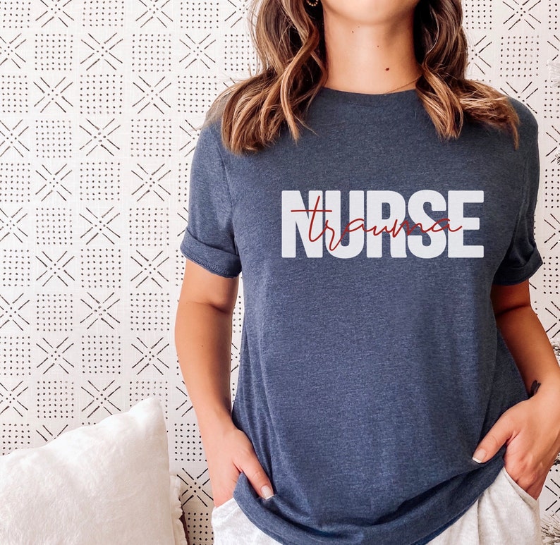 May include: A navy blue t-shirt with the text "NURSE" in white letters and the word "trauma" written in red cursive script underneath.