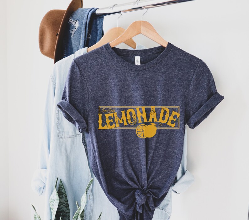 K&ouml;nnte beinhalten: Ein marineblaues T-Shirt mit einer Grafik im Vintage-Stil, auf dem in Gelb "Ice Cold Lemonade" mit einer Illustration einer Zitronenscheibe steht.