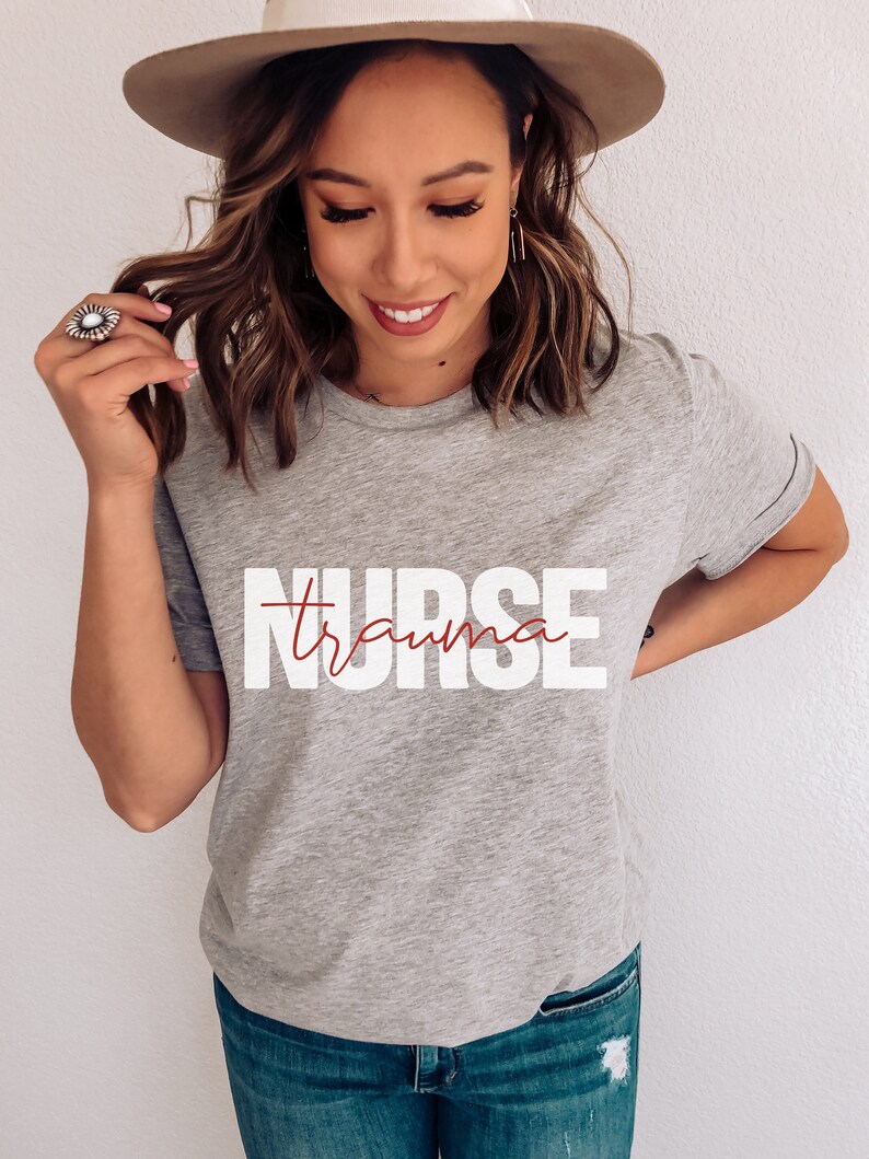 May include: A gray t-shirt with the text "NURSE" in white letters and the word "trauma" written in cursive in red letters.